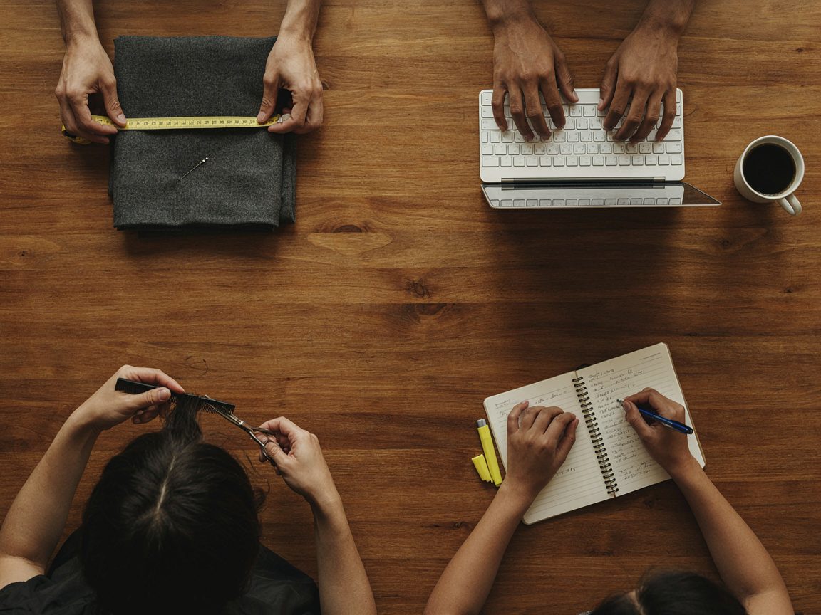 Hands of a tailor, a laptop worker, a hairdresser and a student working side by side at a wooden table