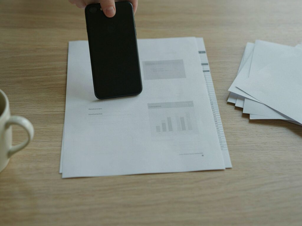 A phone photographing a paper document with a stack of papers beside it